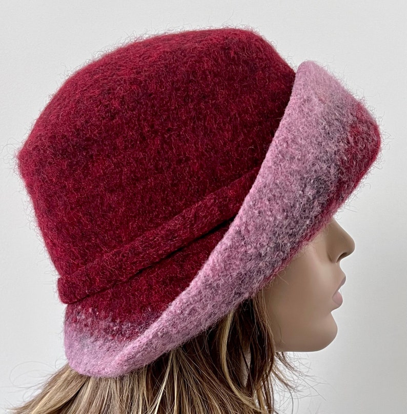 May include: A burgundy and pink wool felt hat with a wide brim. The hat is soft and fluffy, and the brim is turned up on one side.