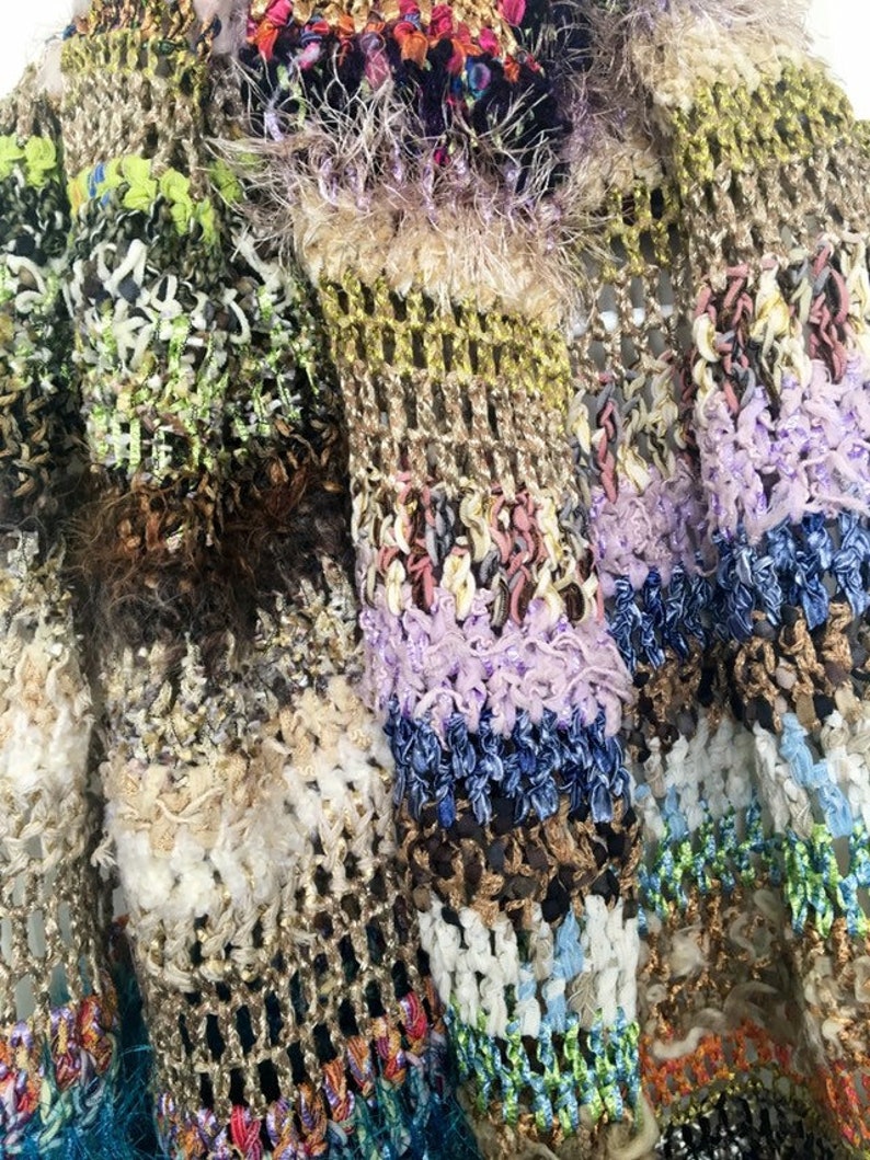 May include: Close-up of a multi-colored crocheted fabric with a variety of textures, including fuzzy, looped, and woven. The fabric is made up of different shades of brown, green, purple, blue, and white.