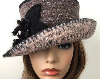 May include: A brown and black wool hat with a black flower accent. The hat has a wide brim and a slightly rounded crown.