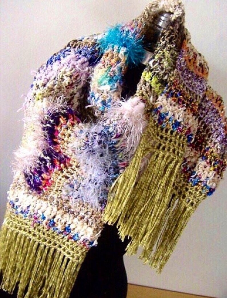May include: A colorful crocheted shawl with a variety of textures and colors, including purple, pink, blue, green, and white. The shawl has long, gold fringe and a fluffy white trim.
