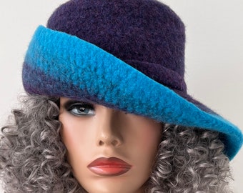 Puede incluir: Un sombrero de fieltro morado y azul con un ala ancha. El sombrero está inclinado hacia abajo sobre la frente del usuario.