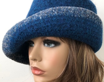 Puede incluir: Un sombrero de fieltro de lana azul con ribete gris. El sombrero tiene un ala ancha y una forma holgada.