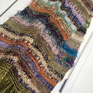 May include: A long, multi-colored crocheted scarf with a fringe. The scarf is made with a variety of yarns in shades of brown, green, orange, purple, blue, and white.
