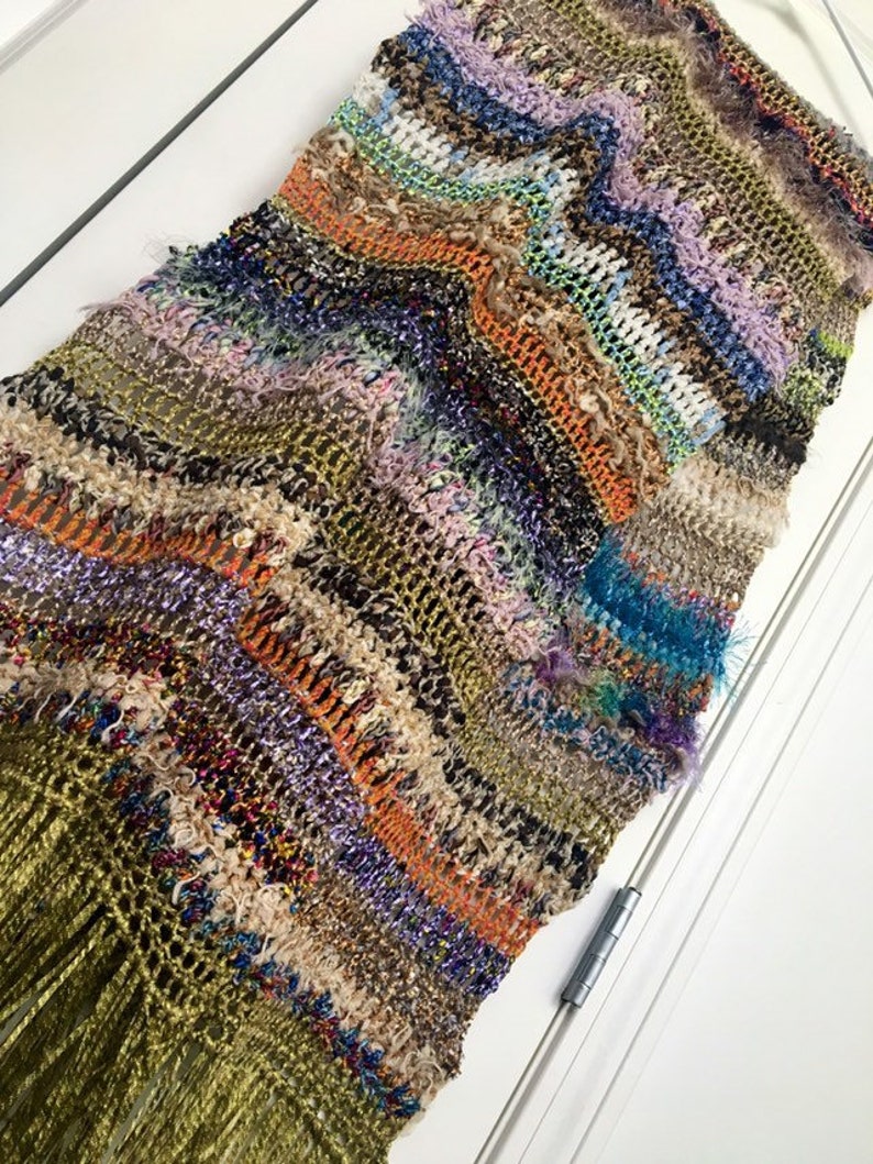 May include: A long, multi-colored crocheted scarf with a fringe. The scarf is made with a variety of yarns in shades of brown, green, orange, purple, blue, and white.