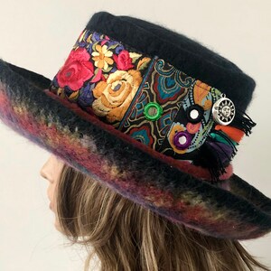 May include: A black felt hat with a wide brim and a colorful floral patterned band. The hat is decorated with a silver sun charm and a few small mirrors.