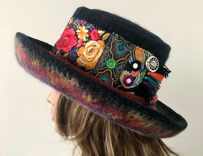 May include: A black felt hat with a wide brim and a colorful floral patterned band. The hat is decorated with a silver sun charm and a few small mirrors.
