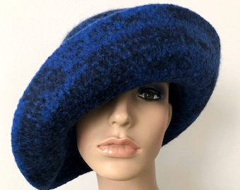 Puede incluir: Un sombrero cloche de fieltro de lana azul y negro con un ala ancha. El sombrero está inclinado hacia un lado, cubriendo un ojo.