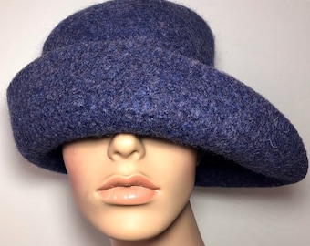 Puede incluir: Un sombrero de fieltro azul con un ala ancha, que cubre los ojos de un maniquí.