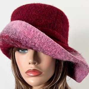 May include: A burgundy and pink felt hat with a wide brim. The hat is made of a soft, fuzzy material and has a unique, asymmetrical design.