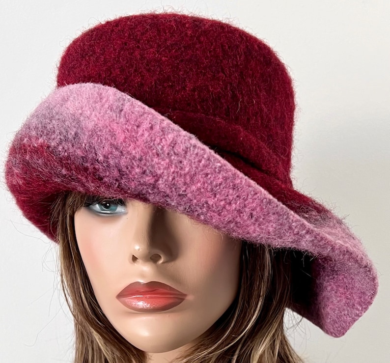 May include: A burgundy and pink felt hat with a wide brim. The hat is made of a soft, fuzzy material and has a unique, asymmetrical design.