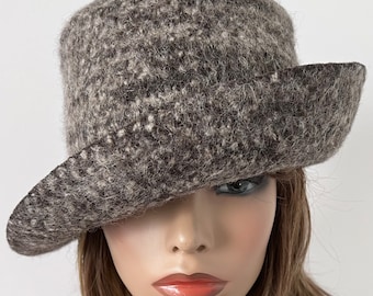 May include: A brown and gray wool felt hat with a wide brim. The hat is angled down over the wearer's face, obscuring one eye.