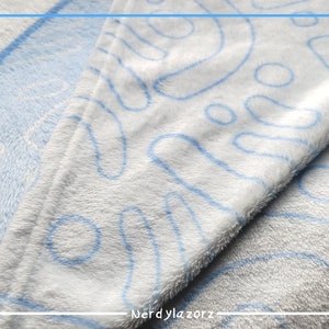 May include: A white blanket with a light blue abstract design. The blanket has a soft, plush texture and is folded, showing the pattern. The text "Nerdylazorz" is visible in the bottom right corner.