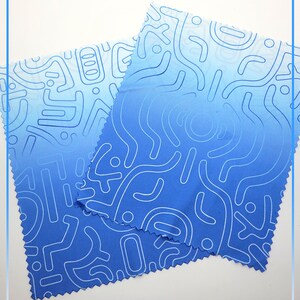 Puede incluir: Dos pa&ntilde;os de limpieza de microfibra azules con un patr&oacute;n abstracto blanco. Los pa&ntilde;os est&aacute;n doblados uno encima del otro.