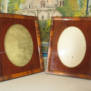 May include: Two antique oval picture frames with ornate wood frames. The frames are made of dark wood with a lighter wood inlay. The frames have brass accents on the corners.
