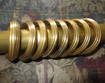 May include: A set of 10 gold-colored metal curtain rings with a decorative ridged design.