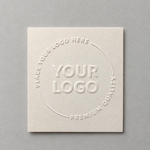 K&ouml;nnte beinhalten: Eine quadratische, cremewei&szlig;e Karte mit einem gepr&auml;gten kreisf&ouml;rmigen Design. Der Text "PLACE YOUR LOGO HERE" ist oben gebogen, w&auml;hrend "PREMIUM QUALITY" der unteren Kurve folgt. In der Mitte stehen die Worte "YOUR LOGO" in fetten Buchstaben.