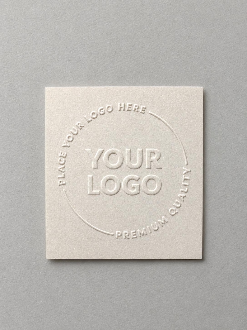 K&ouml;nnte beinhalten: Eine quadratische, cremewei&szlig;e Karte mit einem gepr&auml;gten kreisf&ouml;rmigen Design. Der Text "PLACE YOUR LOGO HERE" ist oben gebogen, w&auml;hrend "PREMIUM QUALITY" der unteren Kurve folgt. In der Mitte stehen die Worte "YOUR LOGO" in fetten Buchstaben.