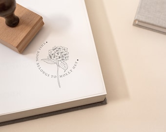 May include: A white book with a black stamp that says "This book belongs to Molly Hey." The stamp features a black and white illustration of a hydrangea flower.