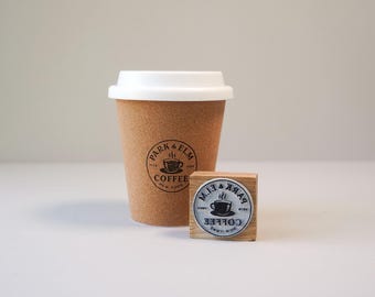 May include: A brown paper coffee cup with a white lid and a wooden stamp. Both items feature the "PARK & ELM COFFEE NEW YORK" logo. The cup is textured, and the stamp is square with a circular design.