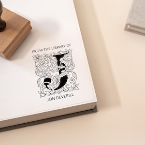 Może przedstawiać: Czarno-biała pieczątka z ozdobną literą J i tekstem "From the Library of Jon Deverill".