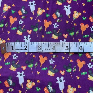 May include: Purple fabric with a repeating pattern of Mickey Mouse heads, candy corn, lollipops, and cupcakes. The fabric is measured with a tape measure that reads "60 inch".