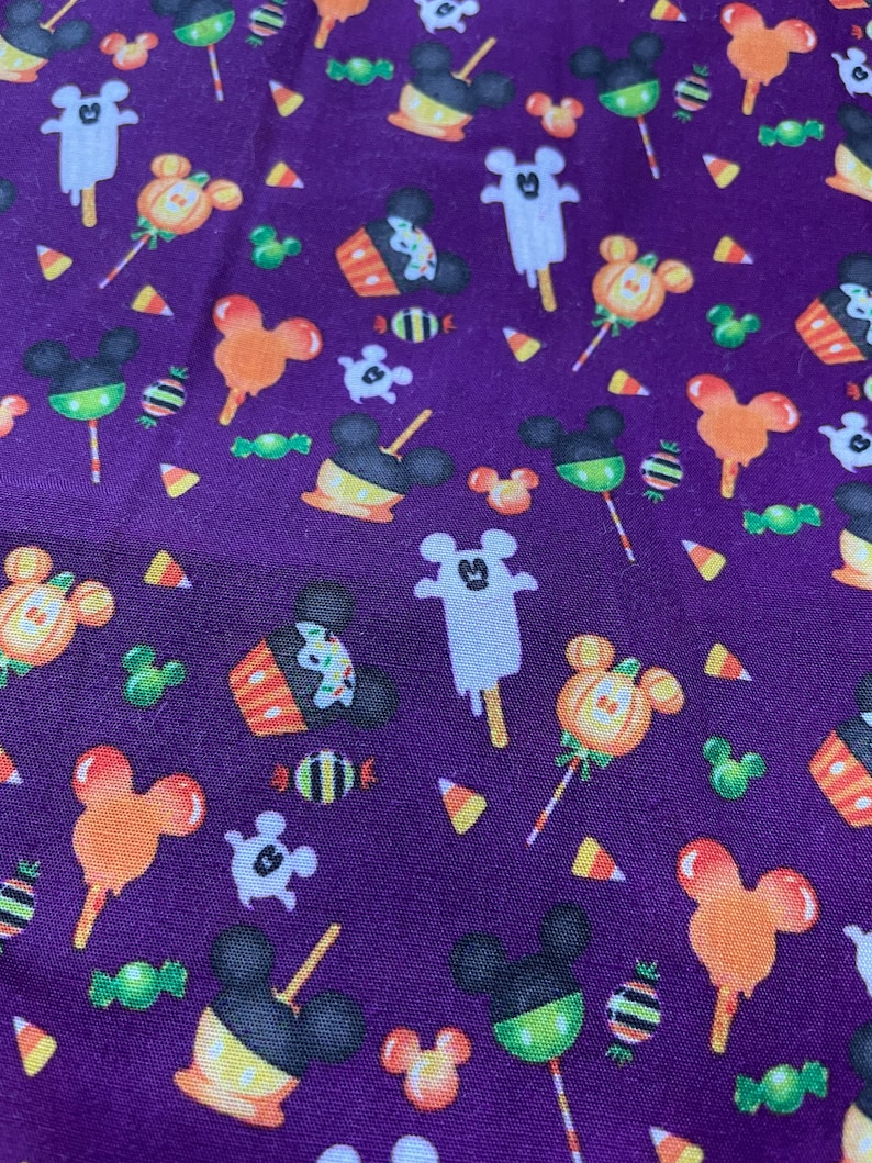 May include: Purple fabric with a repeating pattern of Halloween-themed Mickey Mouse characters. The characters are dressed as ghosts, pumpkins, and candy corn. There are also images of sweets and other Halloween treats.