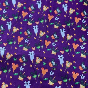 May include: Purple fabric with a repeating pattern of Mickey Mouse heads, ghosts, candy corn, cupcakes, and lollipops. The pattern is in shades of orange, yellow, green, white, and black.