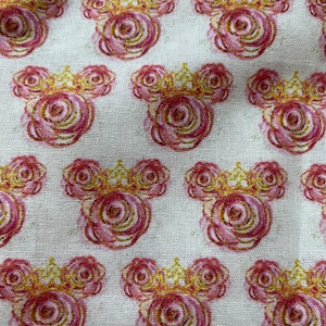 May include: A white fabric with a repeating pattern of pink and gold roses in the shape of a Mickey Mouse head. The roses have a watercolour effect.