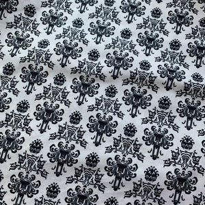 May include: Black and white fabric with a repeating pattern of a ghost with a skull face and a pair of owls. The pattern is on a white background.