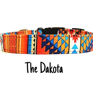 Può includere: Un collare per cani colorato con un motivo geometrico in tonalità arancio, blu e bianco. Il collare è etichettato "The Dakota".