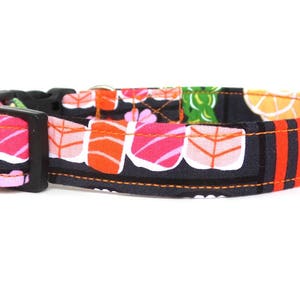 May include: A black dog collar with a colorful sushi print. The collar has a black buckle and orange stitching.