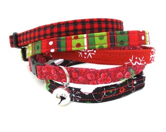May include: A set of four festive cat collars in red, green, black, and white with a bell. The collars feature various holiday patterns, including plaid, snowflakes, and floral designs.