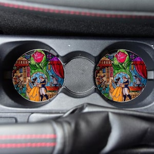 May include: Two colorful car coasters featuring a stained glass style image of Belle and the Beast from the Disney movie Beauty and the Beast.