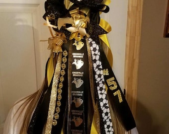 May include: Black and gold hair bow with a large black bow and gold glitter. The bow has black and gold ribbons with the text "Kingsville Brahmas" and a soccer ball pattern. The number "57" is written in gold glitter on a black ribbon.