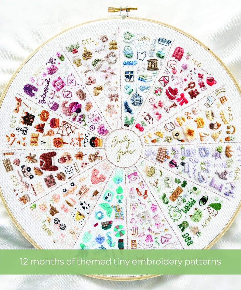 May include: A white embroidery hoop with a colorful embroidery design of 12 months of themed tiny embroidery patterns. The design is in a circle with each month represented by a different color and design. The months are labeled around the circle. The text "Emily June" is in the center of the circle.