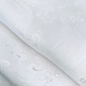 Puede incluir: Tela blanca transparente con un delicado patrón en relieve. La tela tiene un brillo sutil y una textura suave y fluida.