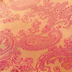 K&ouml;nnte beinhalten: Nahaufnahme eines Stoffes mit Paisley-Muster. Der Stoff ist hellbeige mit einem rosafarbenen Paisley-Muster.