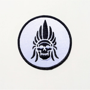 May include: Black and white embroidered patch of a skull wearing a headdress. The patch is circular and has a white background.