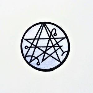 May include: A black and white embroidered patch depicting a five-pointed star with overlapping lines and circles within a circular frame.