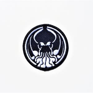 May include: Black and white embroidered patch featuring a stylized depiction of a Cthulhu-like creature with tentacles. The creature is surrounded by a black circle.