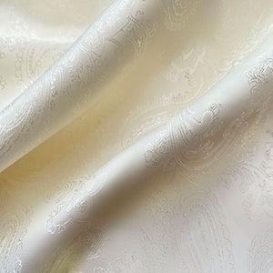 May include: White fabric with a paisley pattern. The fabric is soft and has a subtle sheen.