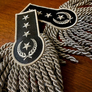 May include: Two black and silver embroidered shoulder boards with silver fringe. The shoulder boards have a star and wreath design.
