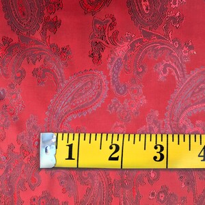 May include: Red paisley fabric with a yellow measuring tape showing 5 inches. The fabric has a subtle sheen and a textured pattern.