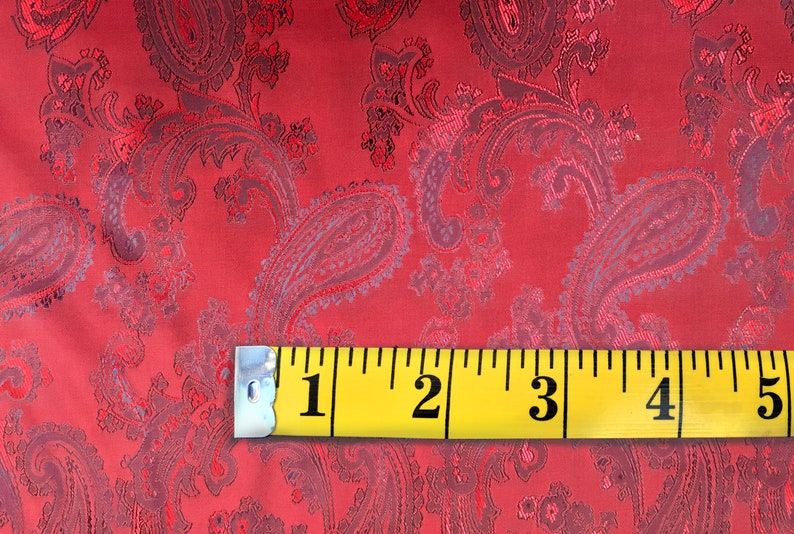 May include: Red paisley fabric with a yellow measuring tape showing 5 inches. The fabric has a subtle sheen and a textured pattern.