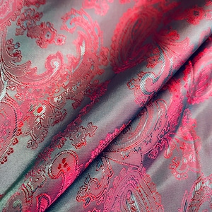 May include: Close-up of a fabric with a paisley pattern in shades of pink and gray. The fabric has a textured, woven look.