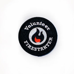 May include: Black and white embroidered patch with the words "Volunteer Firestarter" in a circle around a white flame with an orange center.