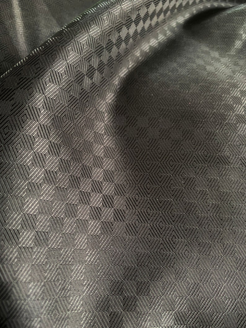 May include: Black fabric with a geometric pattern of small squares. The fabric has a subtle sheen and a textured surface.