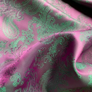 May include: Close-up of a pink fabric with a green paisley pattern. The fabric is soft and has a subtle sheen.