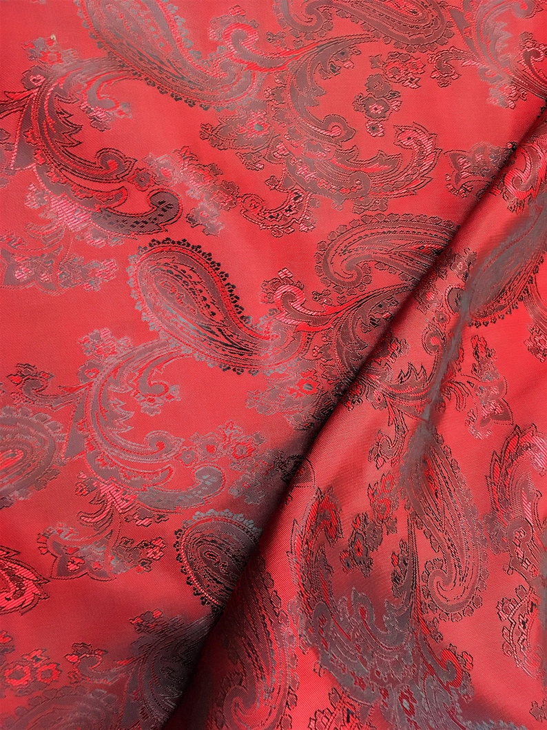 May include: Red fabric with a black paisley pattern. The fabric is folded in half, showing the pattern on both sides.