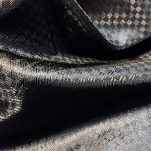 May include: Black fabric with a subtle geometric pattern. The fabric is folded and has a textured surface.